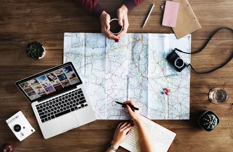 Twee mensen buigen zich over een landkaart, een laptop en een camera om een reis te plannen